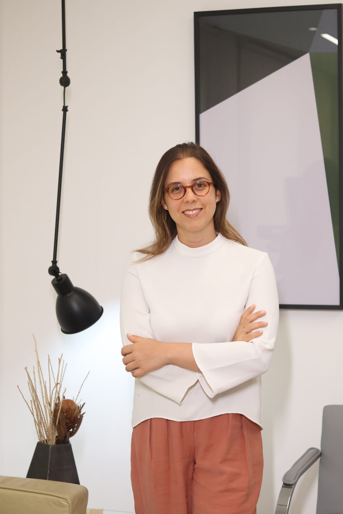 Dra. Ana Flávia Garcia Silva em pé, de braços cruzados, sorrindo em seu consultório